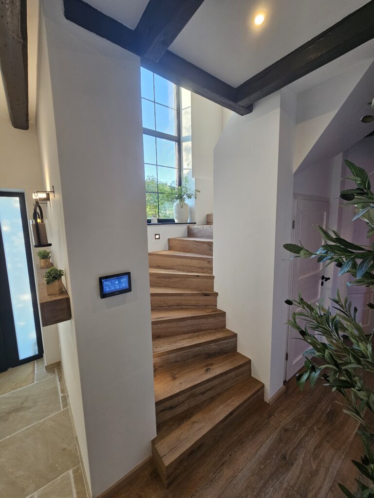Modern sanierte Treppe im Eingangsbereich mit Haustür und Smart-Steuerung an der Wand.
