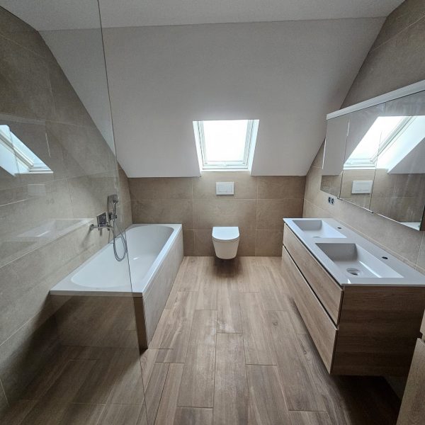 Modern saniertes Badezimmer mit Doppelwaschbecken, Badewanne und Toilette unter dem Fenster.
